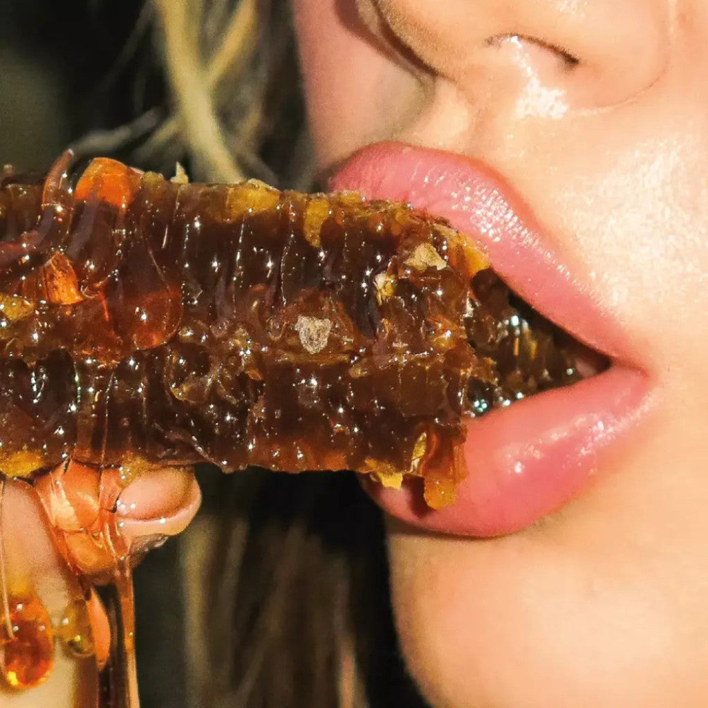 Close-up de mulher comendo favo de mel natural, mel escorrendo nos lábios.
